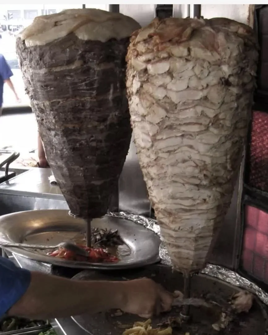 Dois espetos verticais de carne de gyro girando numa lanchonete