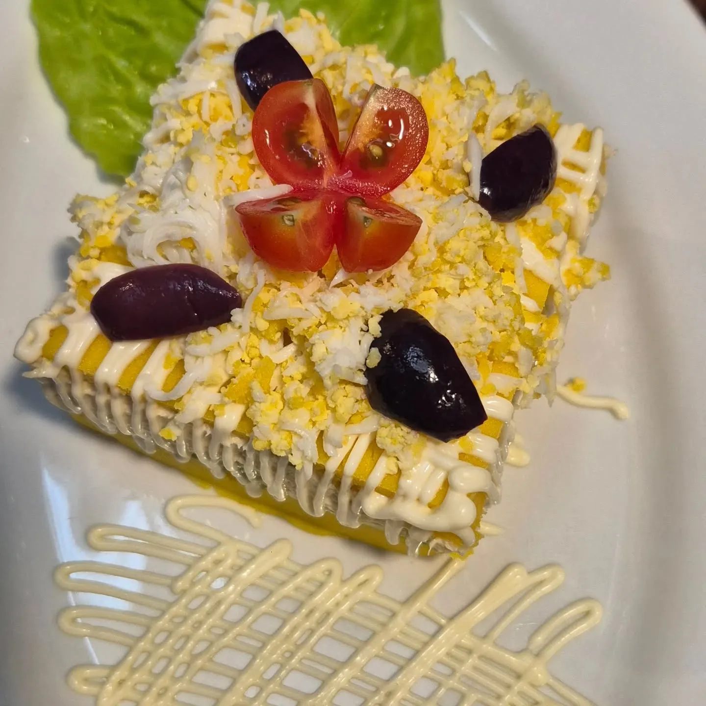 Causa limeña vista de cima, com tomate em flor e azeitonas pretas