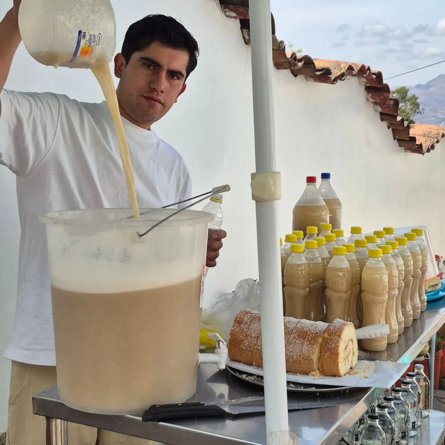 Homem despejando chicha de quinoa num balde, ao lado de garrafas da bebida