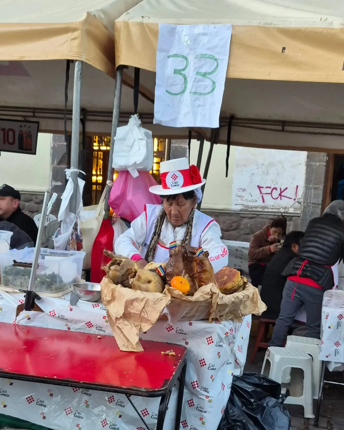 Cozinheira de chapéu numa barraca do festival, com cuys assados e outros pratos