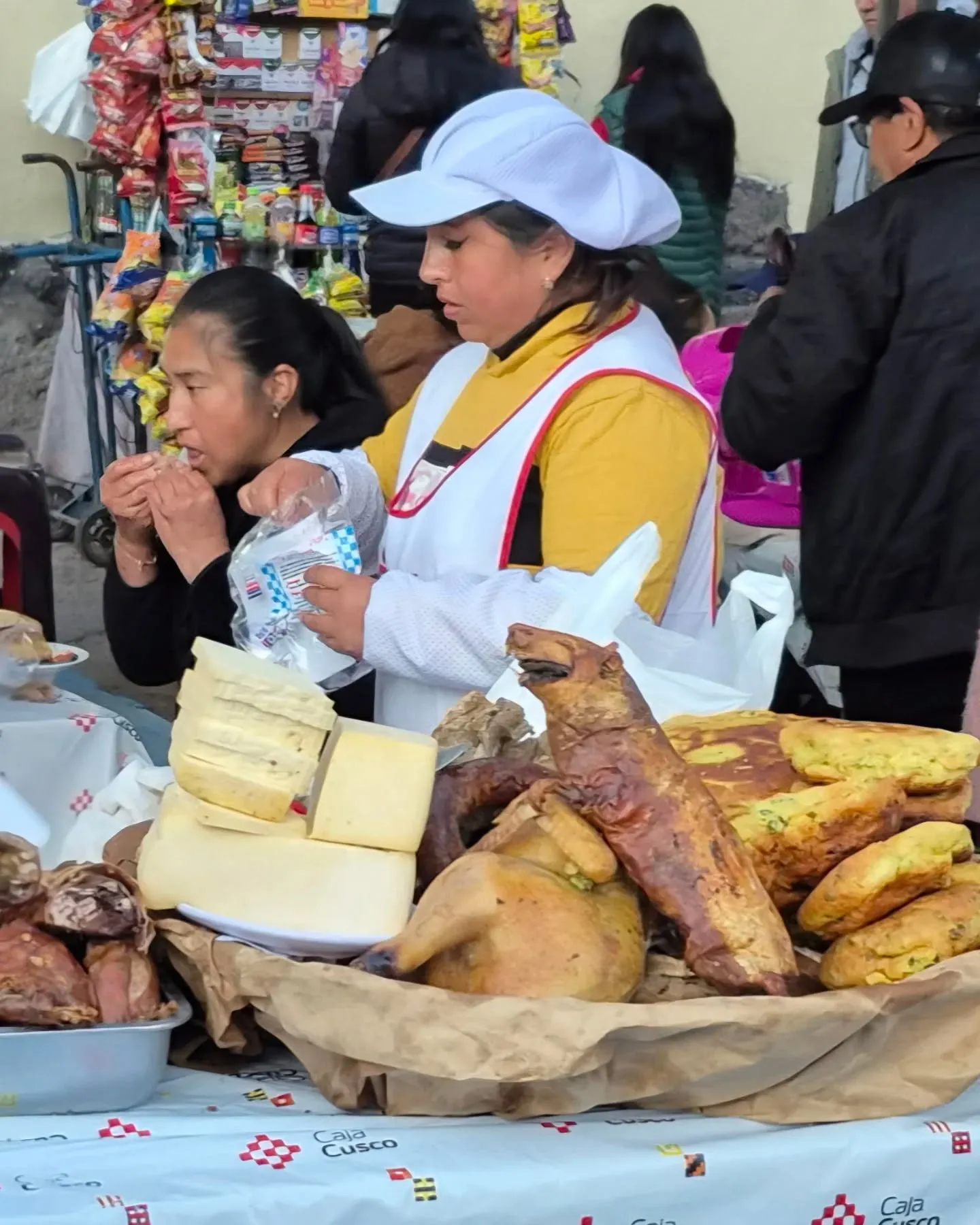 Mulheres numa barraca com queijos, cuys assados e pães fritos