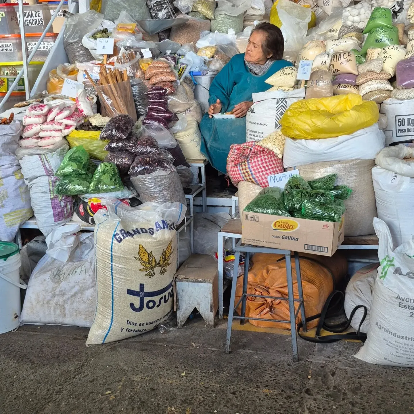 Vendedora sentada entre sacos de grãos, ervas e farinhas no mercado