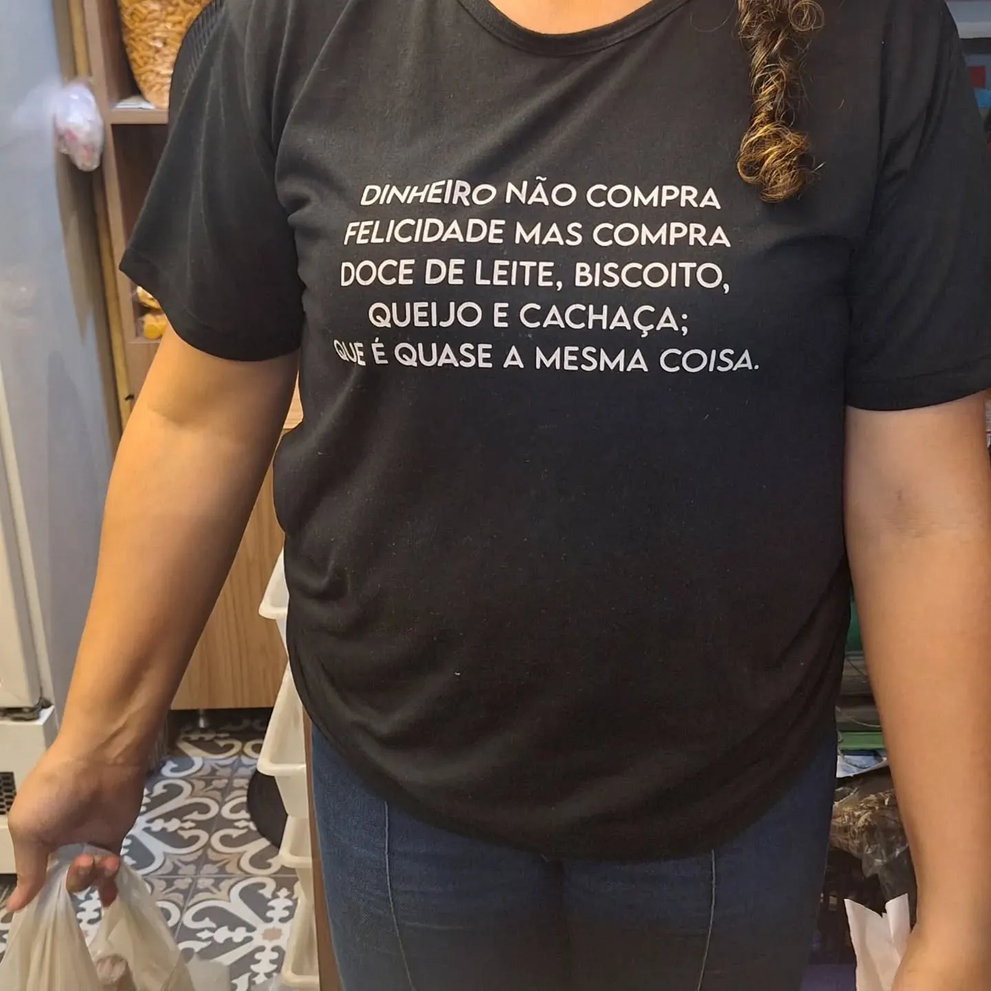 Pessoa de camiseta preta com a frase: dinheiro não compra felicidade mas compra doce de leite, biscoito, queijo e cachaça